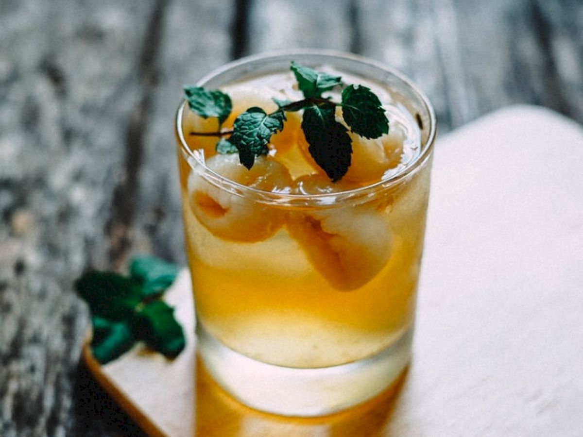 A refreshing cocktail garnished with mint leaves and citrus slices on a wooden board against a rustic wooden background.