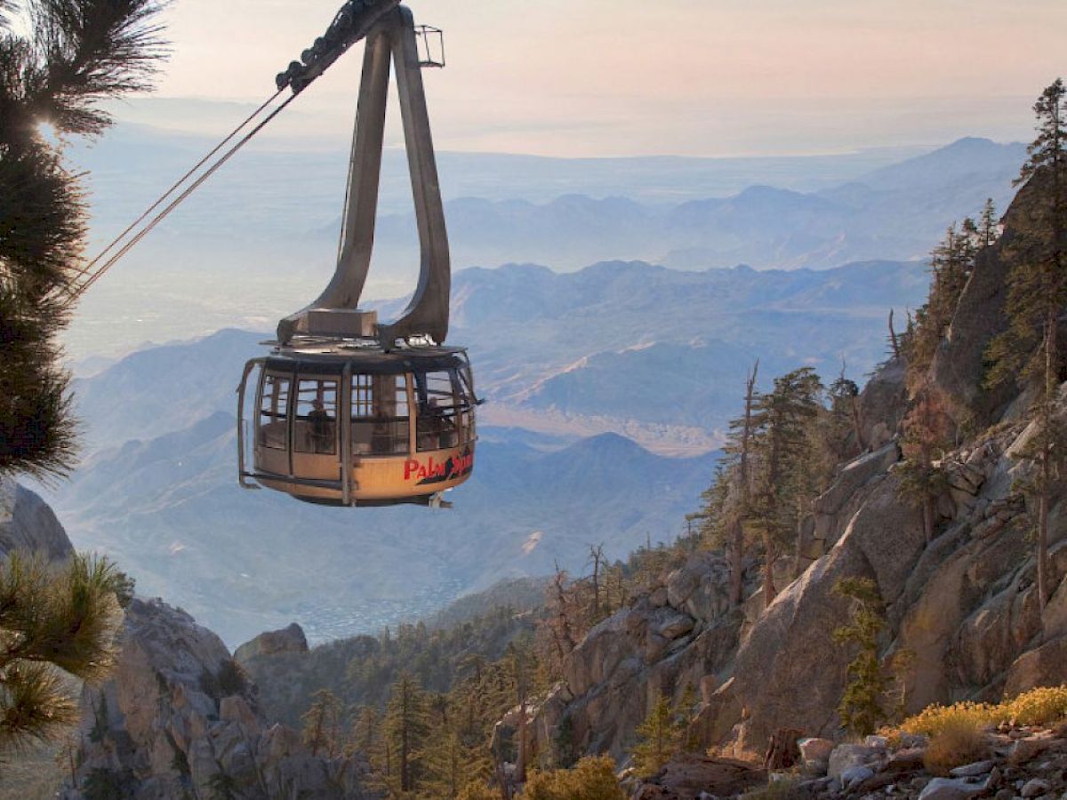 A cable car traverses a mountainous landscape with a scenic view in the background. It is moving between rugged peaks, under a clear sky.