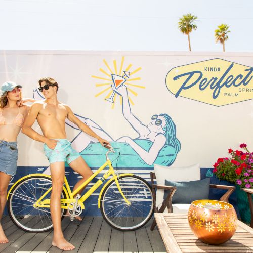 Two people are posing with a yellow bicycle in front of a mural reading 