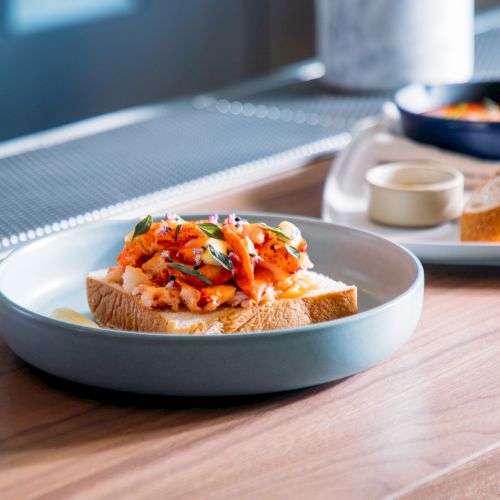 A plate of toast topped with a colorful mixture of vegetables and garnishes is placed on a wooden counter.