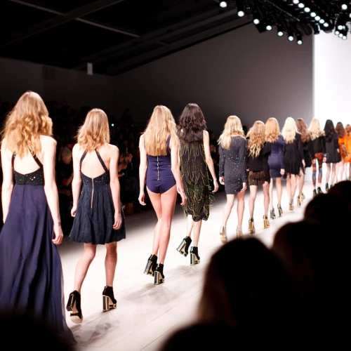 A group of models is walking down a runway during a fashion show. The setting appears professional with bright lights illuminating the scene.