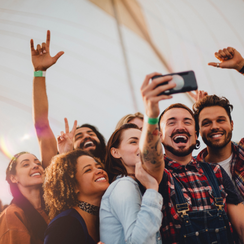 A group of people taking a lively selfie together, smiling and posing enthusiastically at an outdoor event.