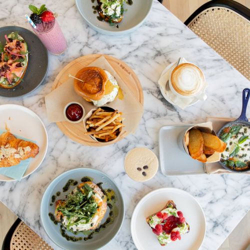 An overhead view of a table with various dishes including burgers, fries, salads, sandwiches, and drinks on a marble table.