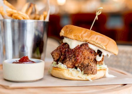 A fried chicken sandwich with lettuce and sauce, accompanied by a metal cup of fries and a small dish of ketchup.