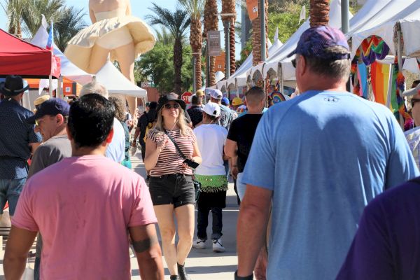 A busy outdoor festival with people walking by tents and a large inflatable decoration in the background.