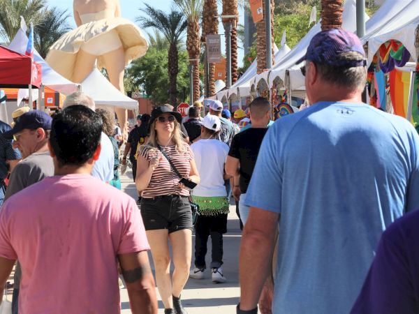 A busy outdoor festival with people walking by tents and a large inflatable decoration in the background.