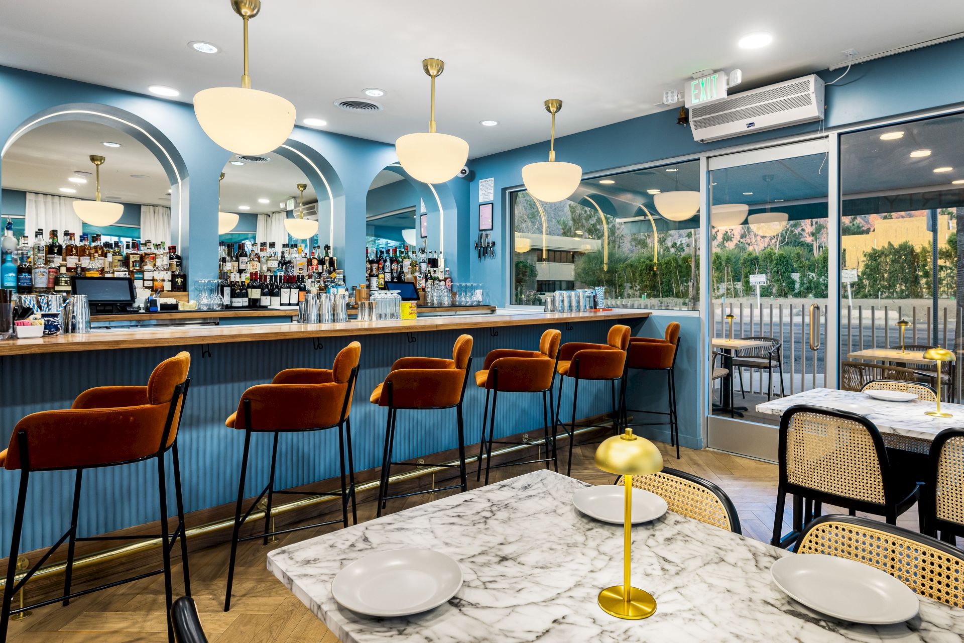 A stylish bar and restaurant with marble tables, red barstools, and modern lighting, offering a cozy atmosphere and a view of the outside.