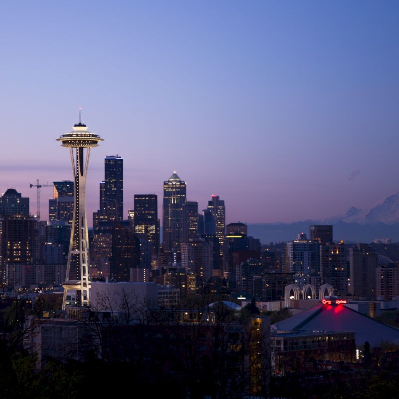 This image shows the Seattle skyline at dusk, featuring the Space Needle prominently with Mount Rainier visible in the background.