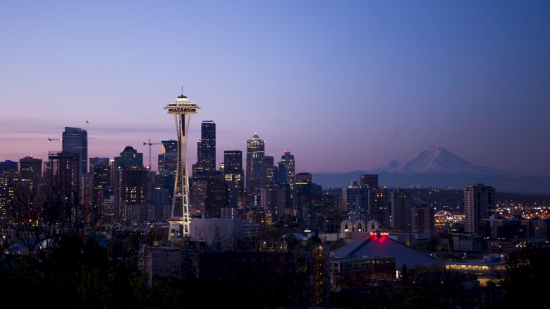 The image depicts a nighttime city skyline featuring the Space Needle with mountains in the background.