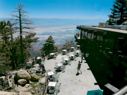 A scenic outdoor café with numerous tables and chairs offering a panoramic view of a valley below, surrounded by trees and rocky terrain, Ending the sentence.