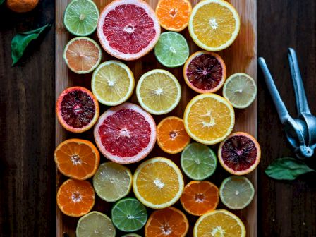 A cutting board with various sliced citrus fruits, including oranges, grapefruit, and limes, arranged neatly. A citrus squeezer is nearby.